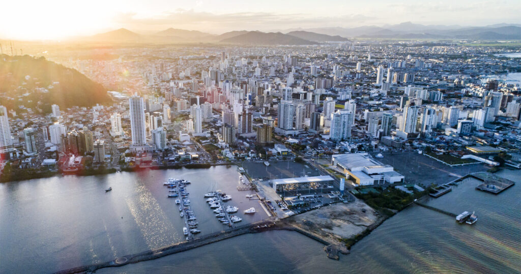 Vista da Praia Brava em Itajaí, com edifícios de luxo e natureza preservada ao fundo, representando o mercado imobiliário de alto padrão.
